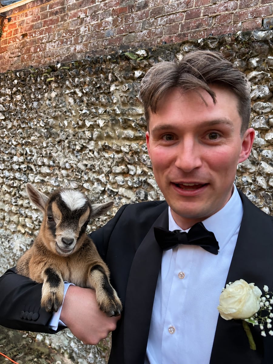Tom Bryant in a tuxedo holding a baby goat